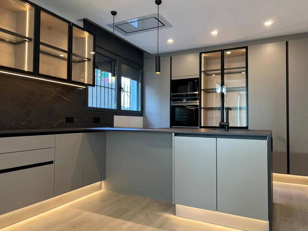 Cocina grande gris con península, vitrinas negras, extractor en techo y luz led en el zócalo